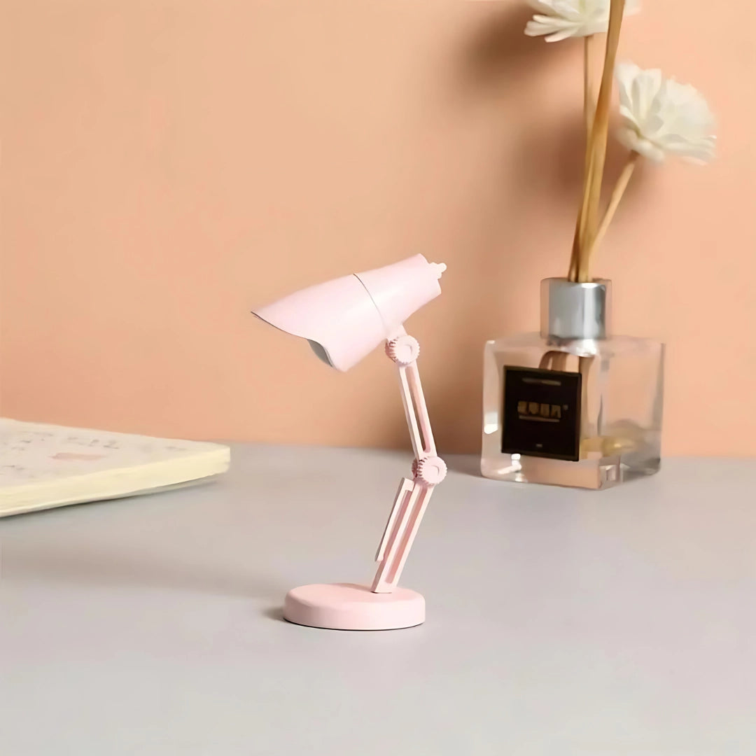 A stylish pink Coral Mini LED adjustable desk lamp with a modern design, featuring a combination of metal and plastic materials, displayed in a room setting.