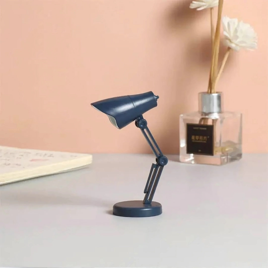 A stylish blue Coral Mini LED Adjustable Desk Lamp positioned on a wooden desk surface in an office or home setting, showcasing its sleek metal design and modern lighting functionality.