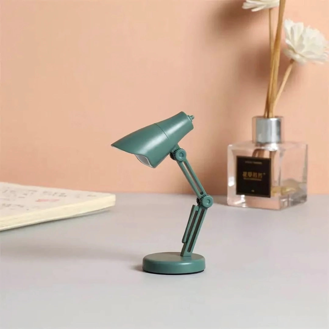 Mini LED desk lamp with a green finish, featuring an adjustable arm and a stylish design, placed on a wooden surface in a room setting.